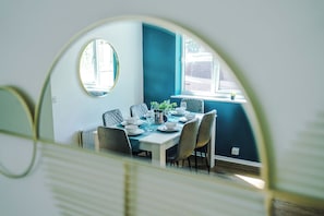 A dining area with a table set for four, a mirror, and a window with a view. - *NEW* Snug 3BR House | FREE Parking | PS4 | Wi-Fi (Greater Manchester)