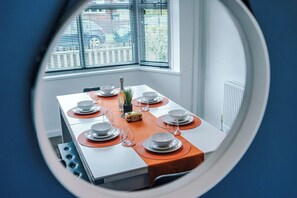 Ein Esstisch mit Tellern, Gläsern und einer Flasche, in einem Raum mit Fenster und Jalousien.