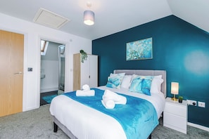 A bedroom with a bed, bedside tables, a nightstand, a wall-mounted lamp, a ceiling light, a door, and a window. - *NEW* Snug 3BR House | FREE Parking | PS4 | Wi-Fi (Greater Manchester)