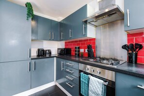 A modern kitchen with grey cabinets, a stainless steel range hood, and red backsplash tiles. - *NEW* Snug 3BR House | FREE Parking | PS4 | Wi-Fi (Greater Manchester)