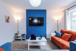 Ein modernes Wohnzimmer mit blauer Akzentwand, einem Flachbildfernseher, einem weißen Couchtisch und einer Couch.
