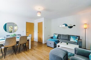 A modern living room with a grey sofa, a dining table with chairs, and a mirror on the wall.