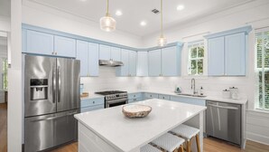 A modern kitchen with stainless steel appliances, light blue cabinets, a central island, and pendant lighting. - Seagrove Home for Groups, Near 30A Beach & Pool (Santa Rosa Beach)
