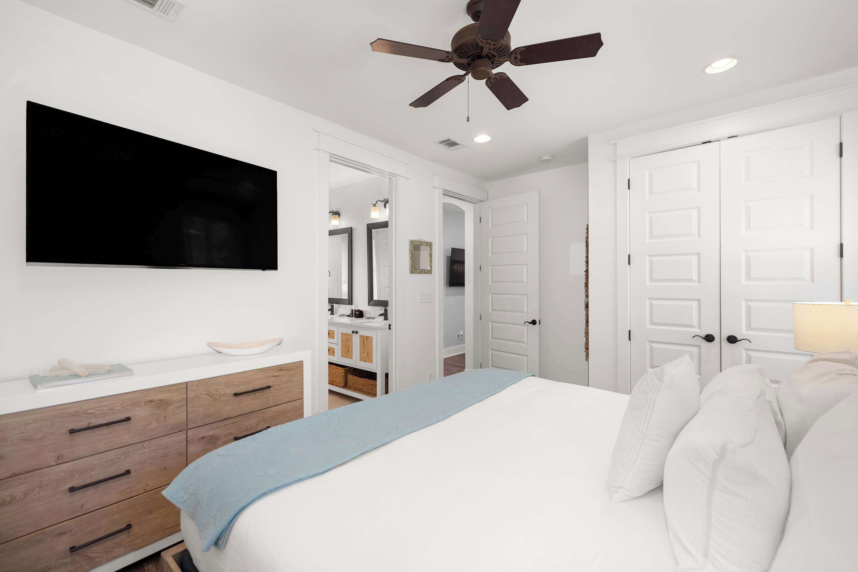 A bedroom with a bed, a ceiling fan, a TV, a dresser, and a closet.