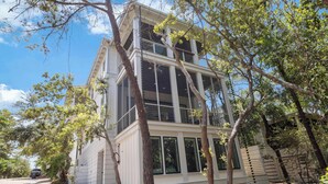Un edificio a due piani con ampie finestre, un balcone e un viale alberato.