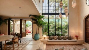 A spacious interior with a large window, a seating area with cushions, a dining table, and a potted plant. - Rooftop Steam Spa, Private Pool & Jungle Retreat (Tulum)