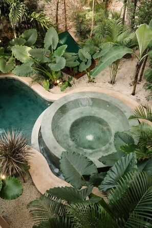 Ein runder Whirlpool, umgeben von üppigen tropischen Pflanzen und einem Schwimmbecken.