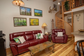A living room with a red leather sofa, a wooden coffee table, and a staircase. - Whetstone Chalet, Golf, Private Lake, XC Ski, Bike trail to Town! (Crested Butte)