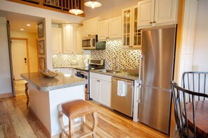 A kitchen with white cabinets, stainless steel appliances, a granite countertop, and a wooden stool. - Whetstone Chalet, Golf, Private Lake, XC Ski, Bike trail to Town! (Crested Butte)