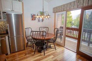 A kitchen with a stainless steel refrigerator, a wooden dining table with four chairs, a hanging light fixture, and a view through a sliding glass door to an outdoor deck. - Whetstone Chalet, Golf, Private Lake, XC Ski, Bike trail to Town! (Crested Butte)