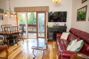 A living room with a red leather couch, a wooden dining table with chairs, a glass-top coffee table, a television, and a fireplace.