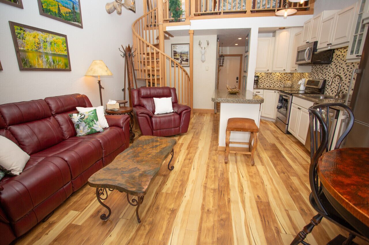 A living room with a red leather sofa, a wooden coffee table, a red armchair, and a bench. There is a staircase leading to an upper level.