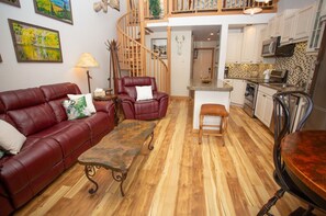 A living room with a red leather sofa, a wooden coffee table, a red armchair, and a bench. There is a staircase leading to an upper level. - Whetstone Chalet, Golf, Private Lake, XC Ski, Bike trail to Town! (Crested Butte)