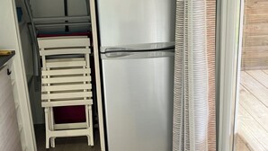 Une cuisine compacte équipée d’un four à micro-ondes et d’un réfrigérateur en acier inoxydable, d’une petite chaise blanche et d’une porte-fenêtre coulissante donnant sur un espace extérieur.