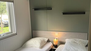 Un petit logement composé d’une seule pièce, comprenant deux lits, une fenêtre et une étagère fixée au mur.