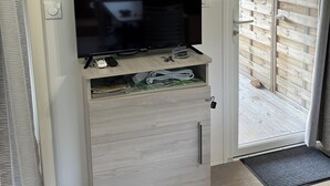 Une pièce dotée d’un téléviseur à écran plat posé sur un meuble en bois, d’une porte-fenêtre coulissante donnant sur l’extérieur et d’un climatiseur fixé au plafond.