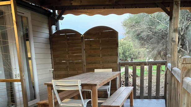Une terrasse en bois avec une table et des chaises, un banc et une chaise longue.