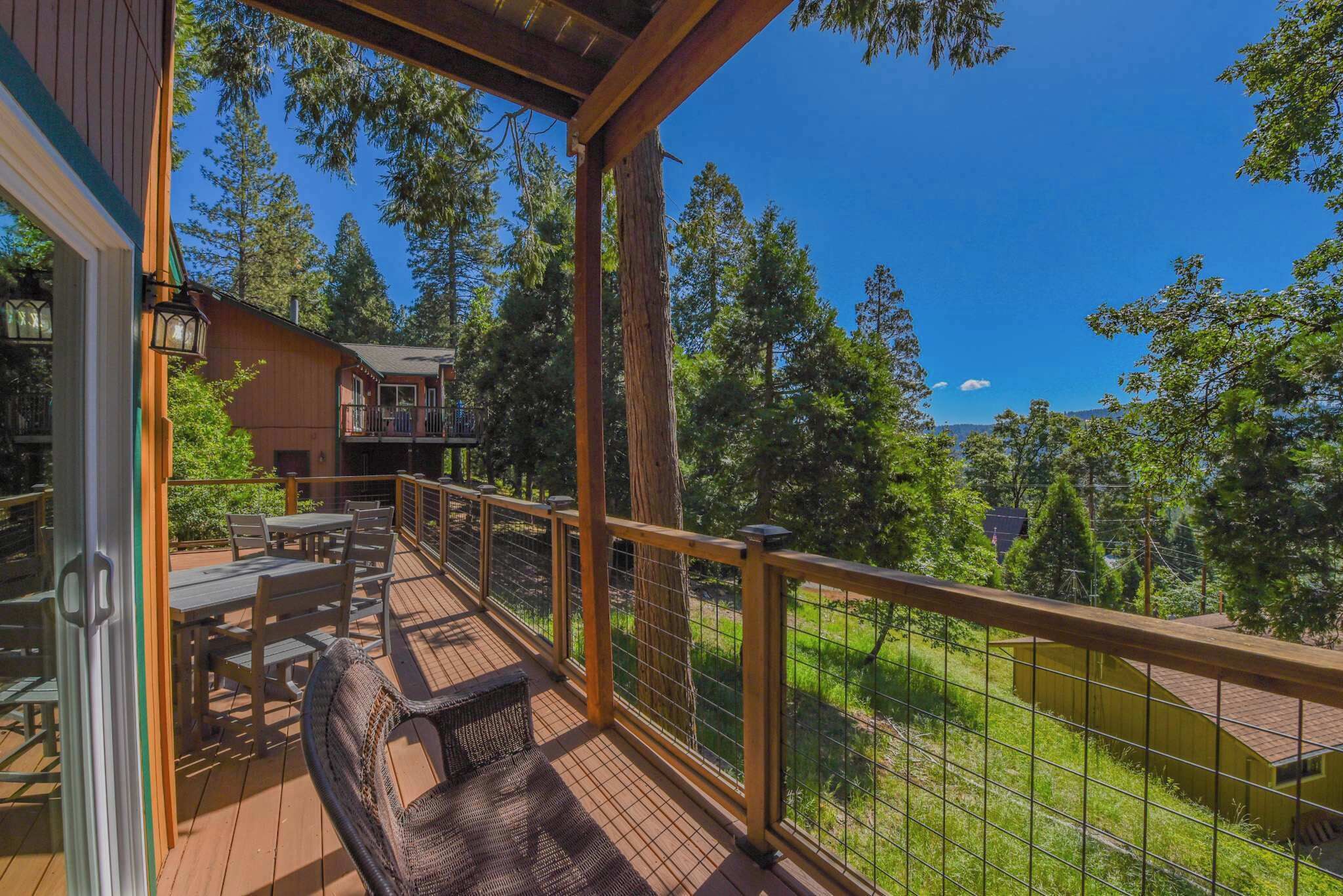 A wooden deck with outdoor furniture, a railing, and a view of trees and a building in the background.