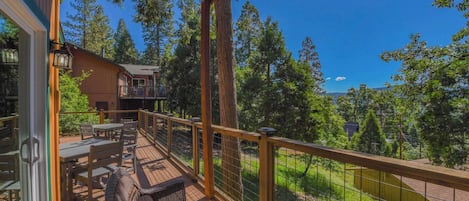 A wooden deck with outdoor furniture, a railing, and a view of trees and a building in the background.
