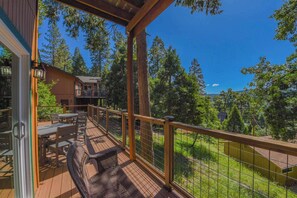 Eine Holzterrasse mit Gartenmöbeln, einem Geländer und Blick auf Bäume sowie ein Gebäude im Hintergrund.