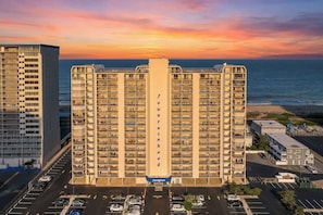 Ein Hochhaus-Hotel mit mehreren Balkonen, einem Parkplatz und Blick auf das Meer bei Sonnenuntergang.