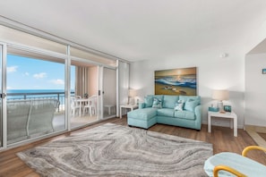 Ein Wohnzimmer mit Sofa, einem Gemälde, einem Tisch und Meerblick durch große Schiebetüren.