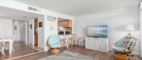 A modern living room with a dining area, kitchen, and a large painting on the wall.