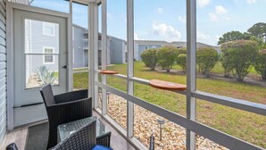 Eine überdachte Veranda mit Korbmöbeln, einer Tür zum Garten und Blick auf Nachbarhäuser und Grünflächen.