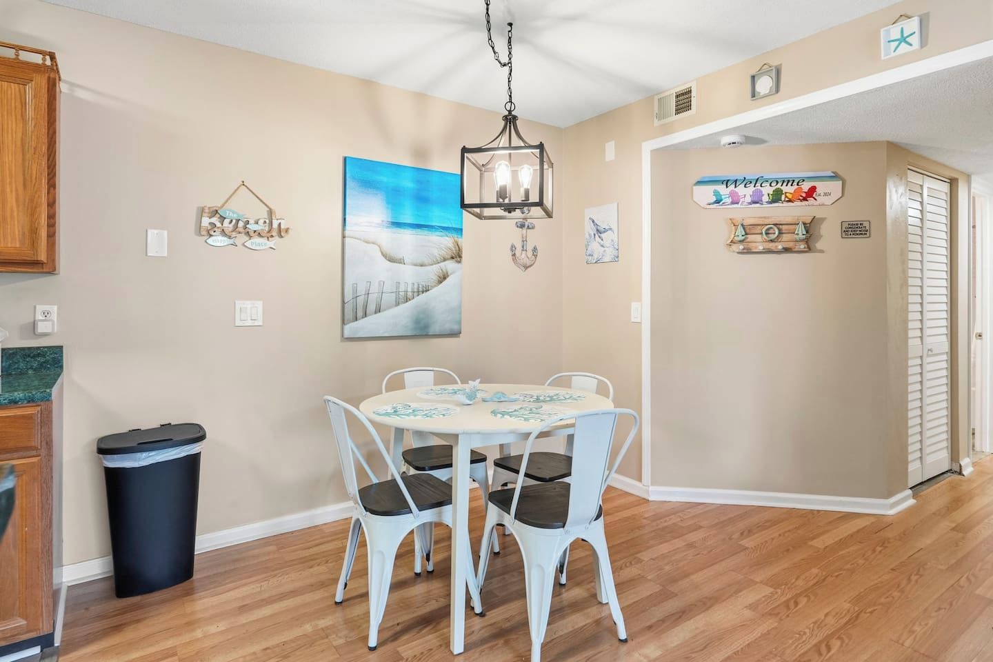 A dining area with a round table, white chairs, and a painting of a snowy landscape.