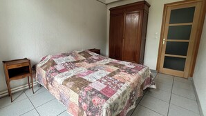 Ein Schlafzimmer mit einem Bett, einem Holzschrank, einem kleinen Nachttisch und einem Fliesenboden.