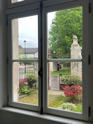 A window with a view of a garden, a stone structure, and a street.