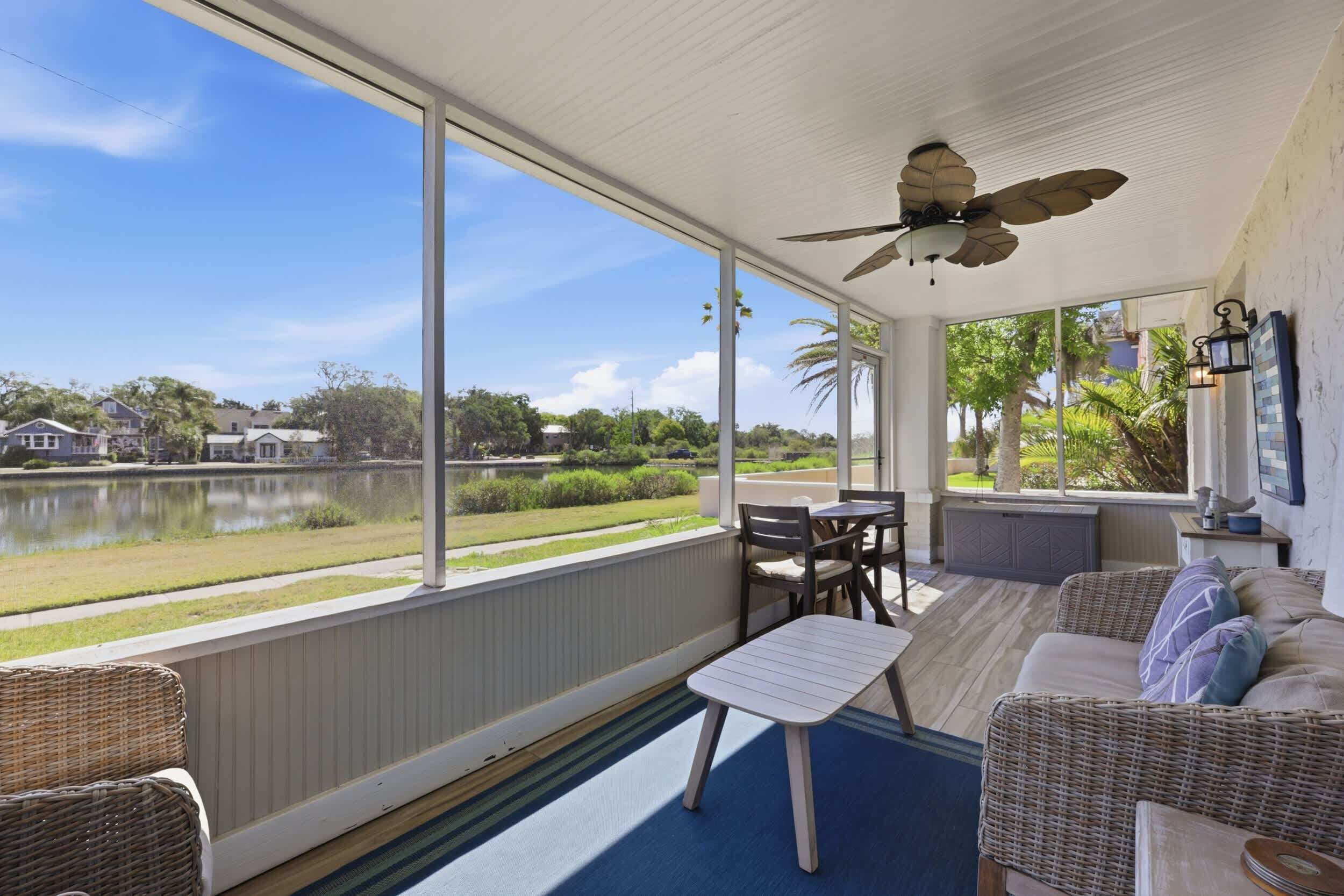 A covered outdoor area with a table and chairs, a ceiling fan, and a view of a lake and houses.