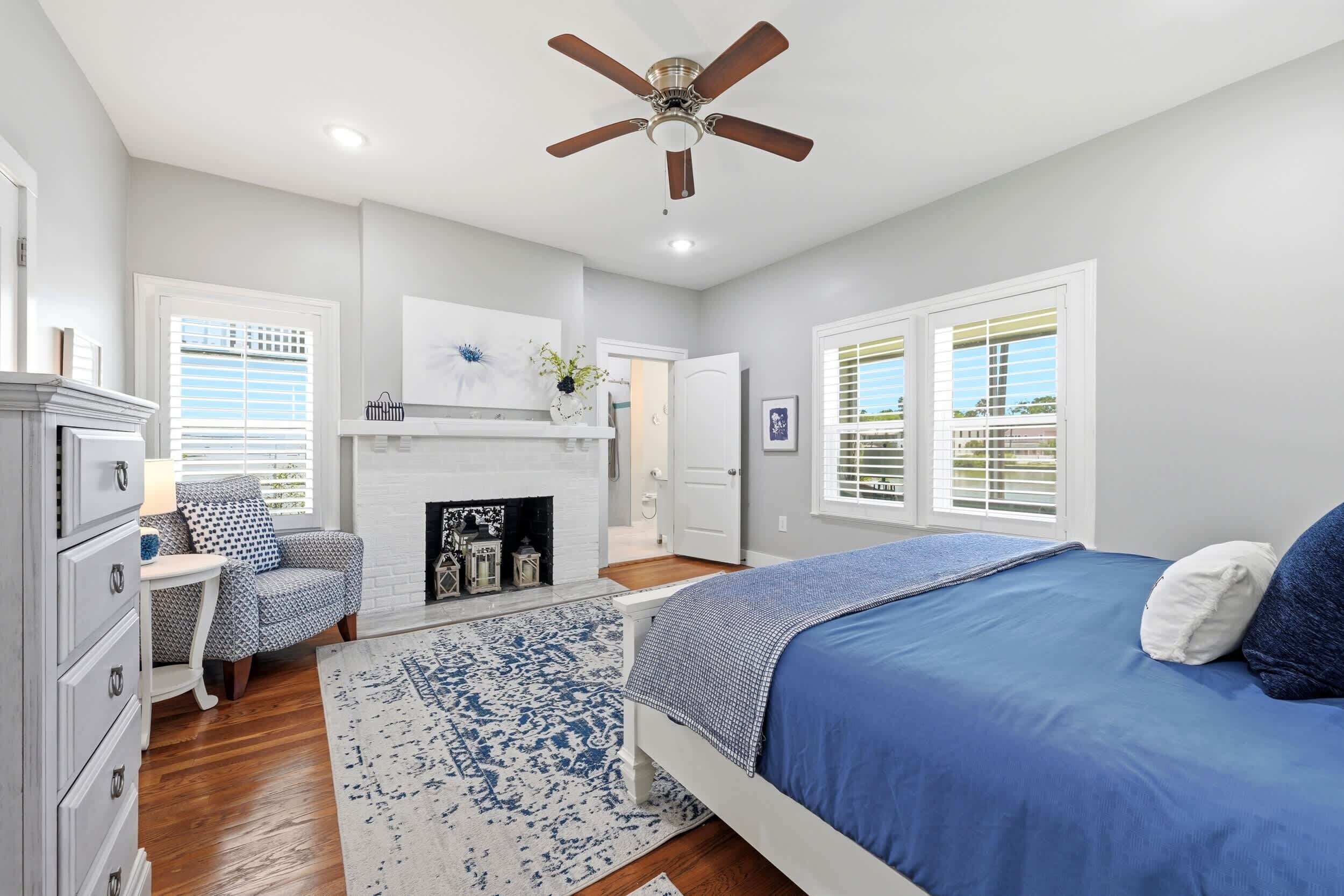 A bedroom with a bed, a fireplace, a ceiling fan, and a window with blinds.