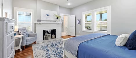 A bedroom with a bed, a fireplace, a ceiling fan, and a window with blinds.