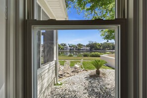 Blick durch ein Fenster auf ein Haus mit Terrasse, Sitzgelegenheit im Freien und einen kleinen Garten.