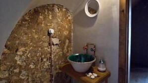 A bathroom with a rustic stone wall, a wooden shelf with a bowl, a hanging light, and patterned tiles. - una volta antica dimora del 1500 B&B (Cava de' Tirreni)