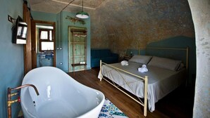 A bedroom with a large bathtub, a bed, and a hanging light fixture. - una volta antica dimora del 1500 B&B (Cava de' Tirreni)