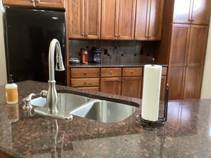 A kitchen with a double sink, wooden cabinets, a black refrigerator, and a coffee maker.