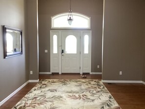 A hallway with a floral carpet, a white door with two windows, and a hanging light fixture.