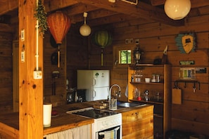 Een rustiek houten interieur van een chalet, met een keuken voorzien van een fornuis, koelkast en houten keukenkastjes.