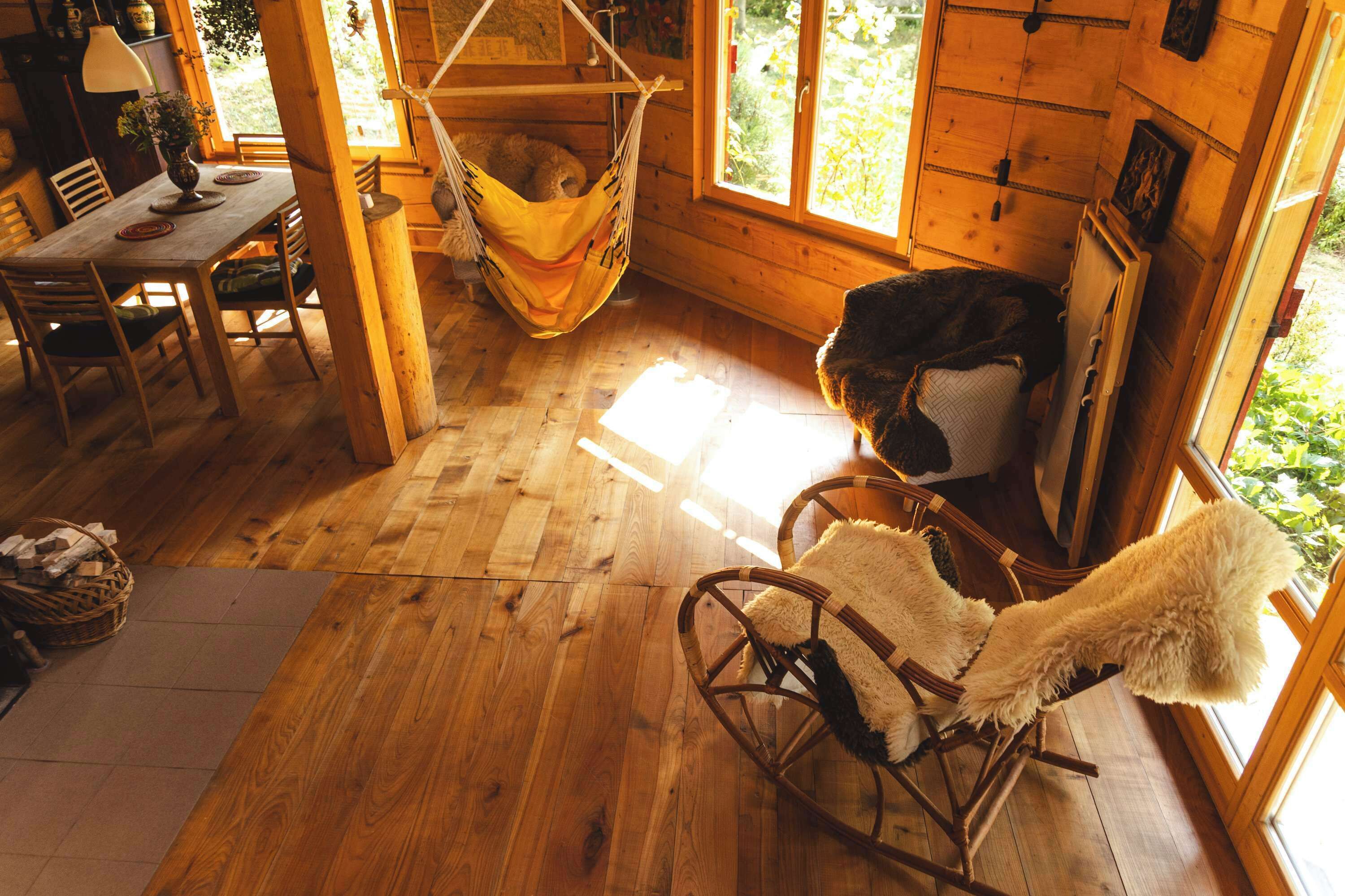 A cozy cabin interior with a wooden floor, a rocking chair, a hammock, and a dining area with a table and chairs.