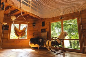 A wooden cabin interior with a hammock, rocking chair, and large windows offering a view of the outdoors. - Bukowica Miła - Nature Escape with eco sauna (Wola Piotrowa)