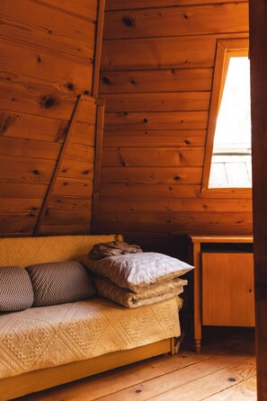 A wooden cabin interior with a bed, pillows, and a window.