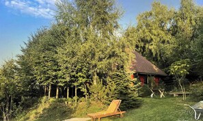 Ein rustikales Blockhaus, umgeben von dichtem Wald, einem Holzstuhl und einem kleinen Garten.