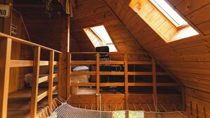 A wooden attic room with skylights, a bunk bed, and a small desk.