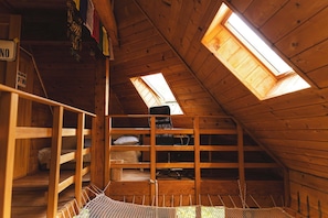 Een houten zolderkamer met dakramen, een stapelbed en een klein bureau.