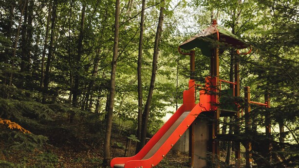 A playground with a red slide and a climbing structure in a forested area.