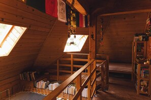 A cozy attic room with a sloped ceiling, wooden beams, a bunk bed, a small desk with a chair, a bookshelf, and a window with a view.