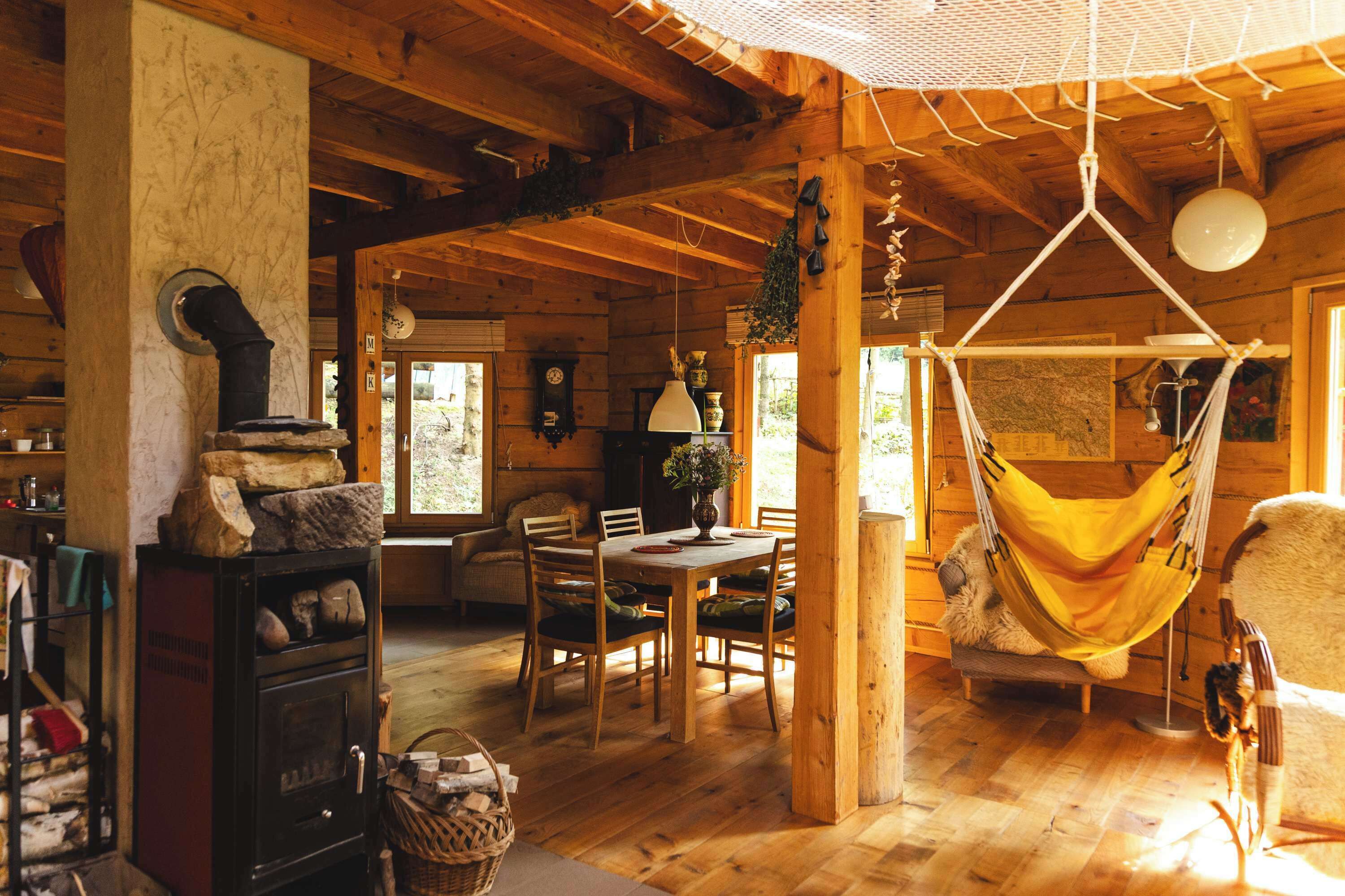 Interior rústico de uma cabana de madeira, com área de refeições, uma rede e uma lareira.
