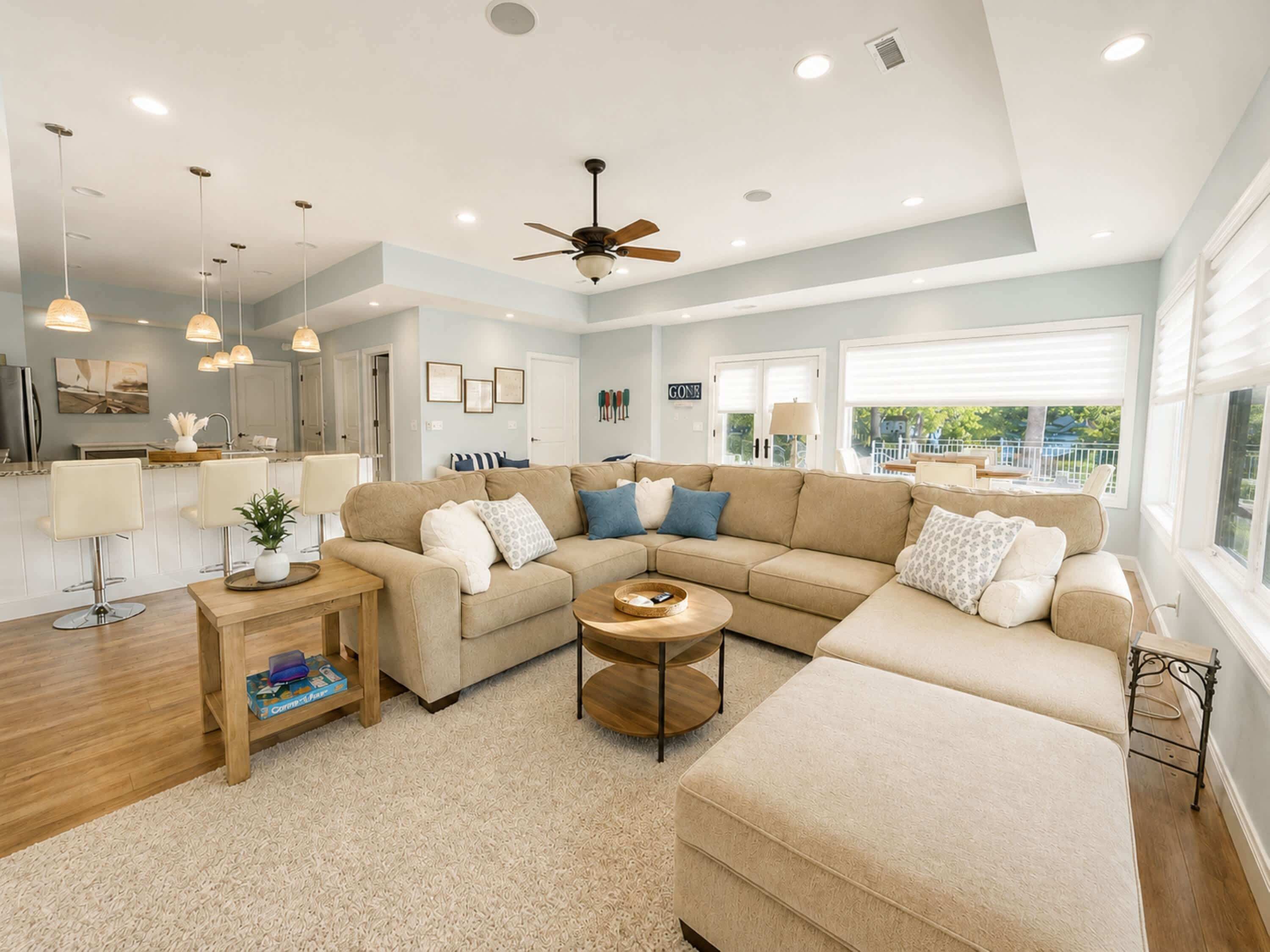 A spacious living room with a large beige sectional sofa, a wooden coffee table, pendant lights, and a ceiling fan.